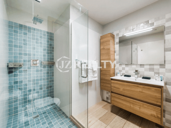 Spacious bathroom in Porta al Sole Unit 18 with a floating wood vanity, dual sinks, a large walk-in shower with turquoise subway tile, and light gray patterned wall tile.