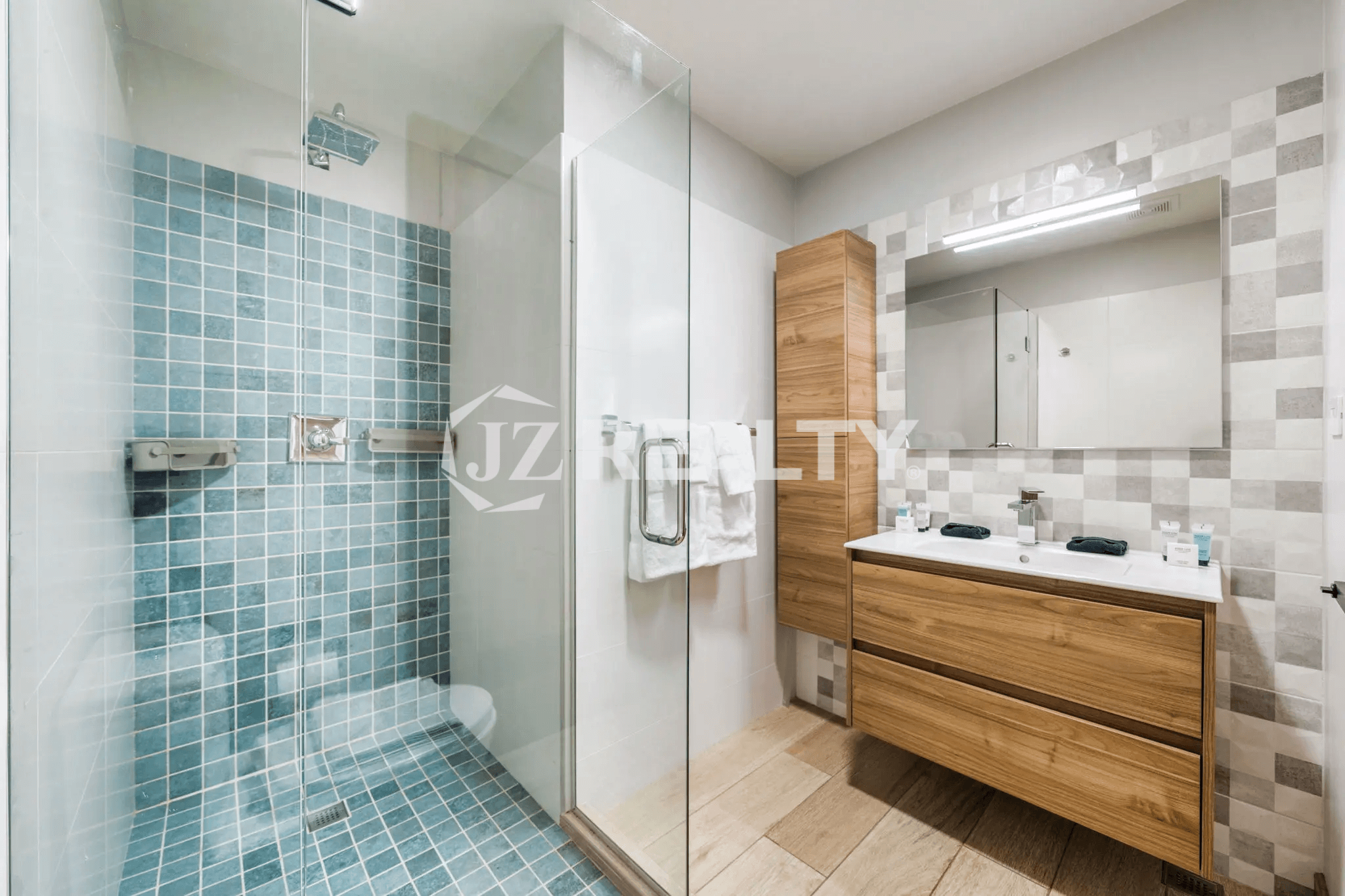Spacious bathroom in Porta al Sole Unit 18 with a floating wood vanity, dual sinks, a large walk-in shower with turquoise subway tile, and light gray patterned wall tile.