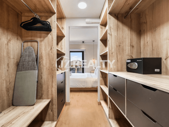 Walk-in closet in the primary bedroom of Porta al Sole Unit 18, featuring wood-tone shelving, drawers, hanging space, a safe box, and an ironing board.