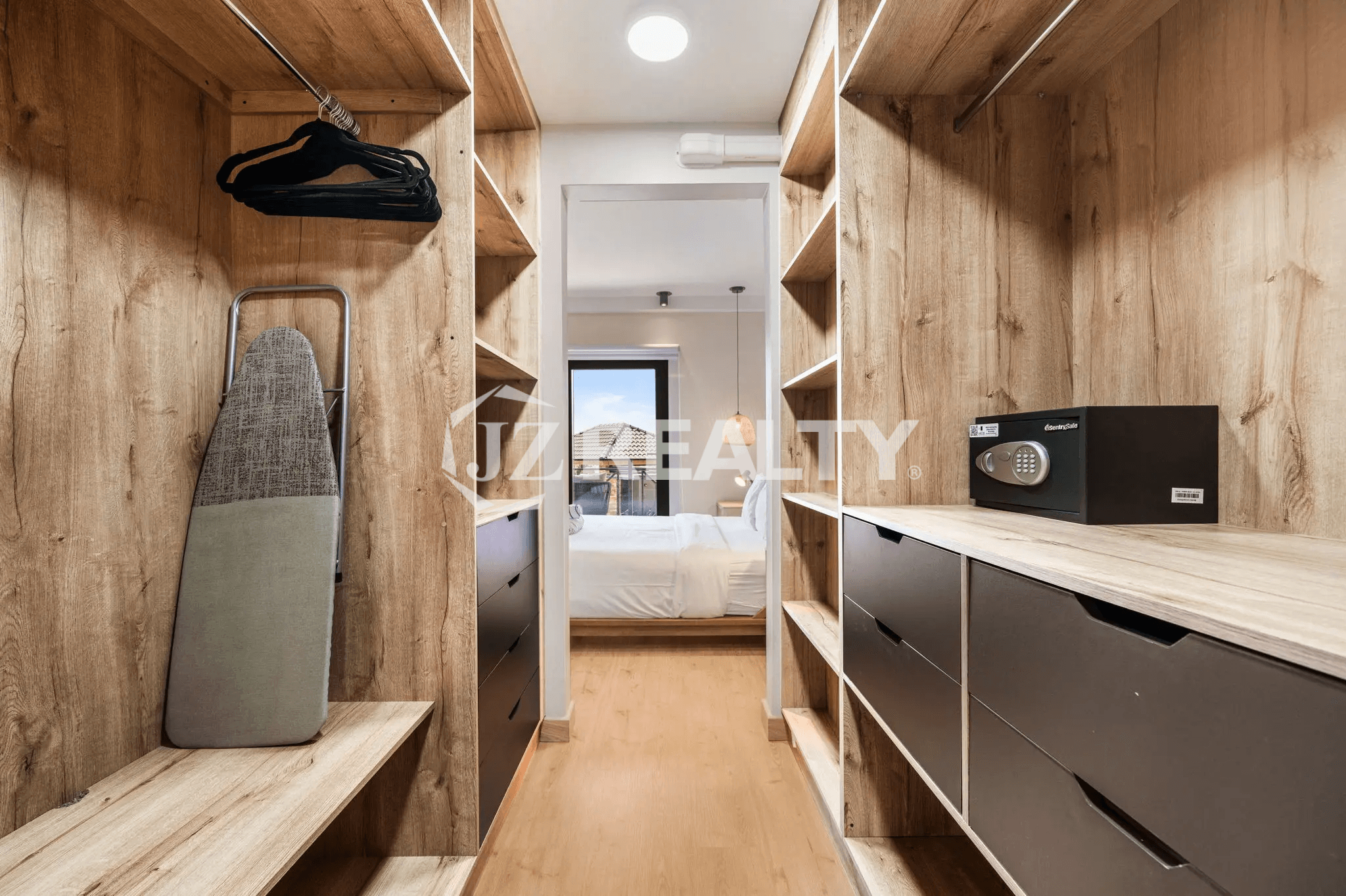Walk-in closet in the primary bedroom of Porta al Sole Unit 18, featuring wood-tone shelving, drawers, hanging space, a safe box, and an ironing board.