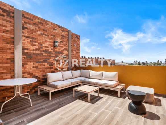 Modern outdoor lounge area on the rooftop terrace of Porta al Sole Unit 18 with a large white cushioned sectional sofa, coffee table, and exposed brick accent wall.