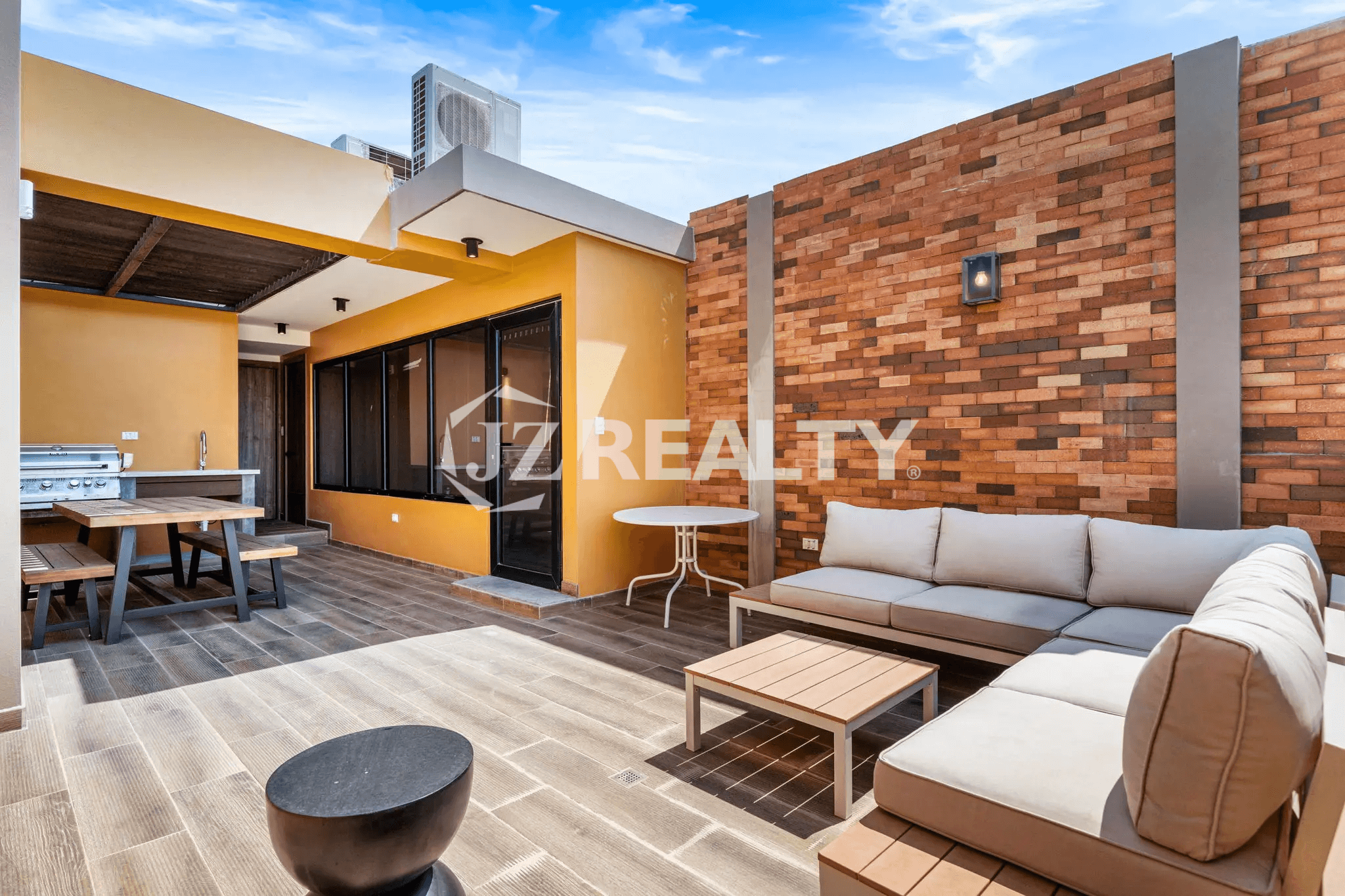 Spacious rooftop terrace at Porta al Sole Unit 18 featuring an outdoor kitchen/grill area, a large sectional seating area with cushions, and sun-drenched wood-look tile flooring.