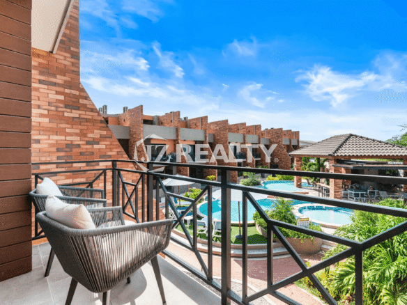 View from the private terrace balcony of Porta al Sole Unit 18, showing a seating area and an expansive view of the community's tropical pool and surrounding brick architecture.