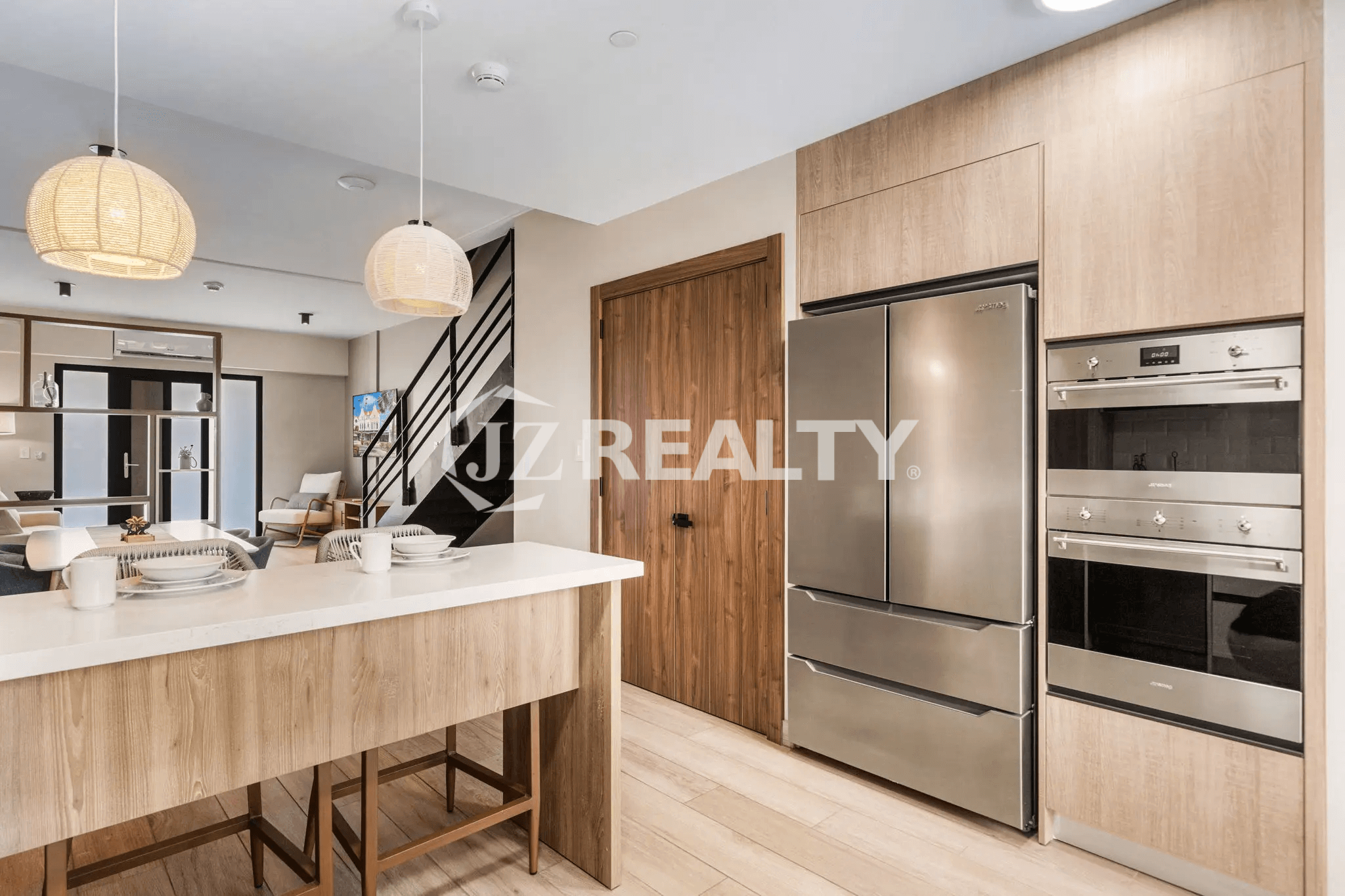 Modern kitchen in Porta al Sole Unit 18 featuring light wood cabinets, stainless steel refrigerator, built-in oven, white countertop island, and rattan pendant lights.