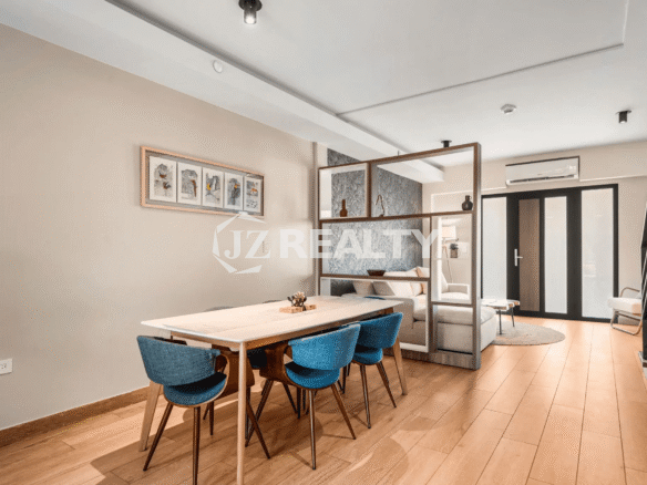 Dining area in Porta al Sole Unit 18 with a long white table, six blue chairs, and a decorative open shelving unit dividing the space from the living room.