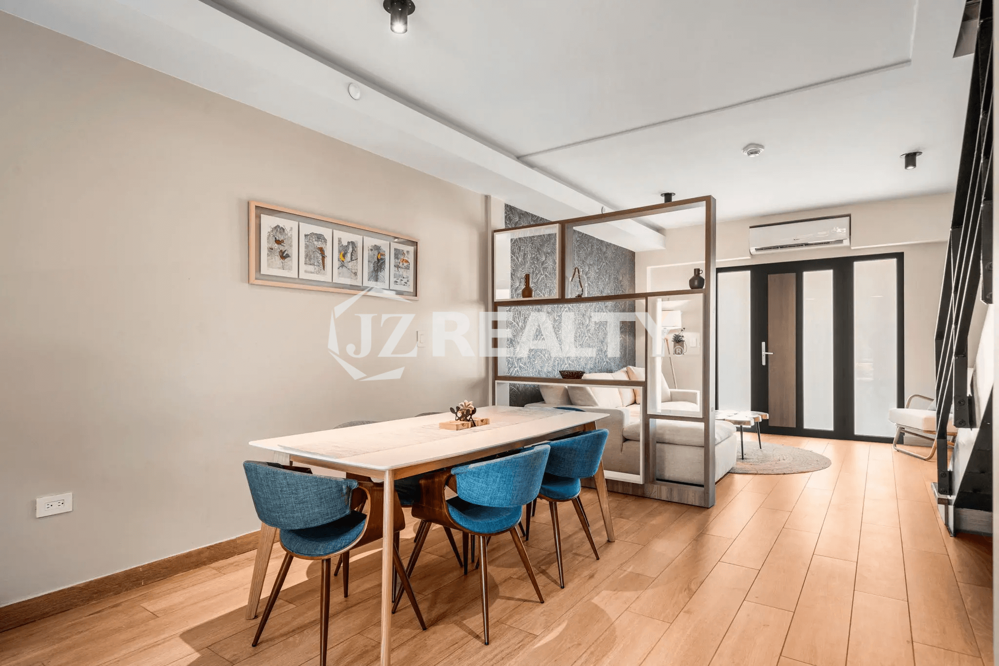 Dining area in Porta al Sole Unit 18 with a long white table, six blue chairs, and a decorative open shelving unit dividing the space from the living room.