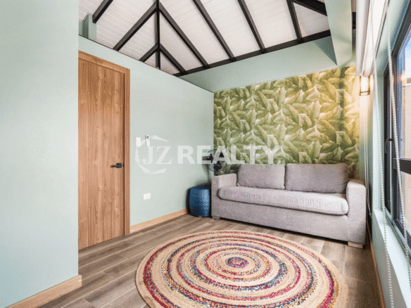 Cozy third-floor sitting room in Porta al Sole Unit 18 with a pull-out sofa, tropical leaf-patterned accent wallpaper, vaulted ceiling, and colorful circular rug.