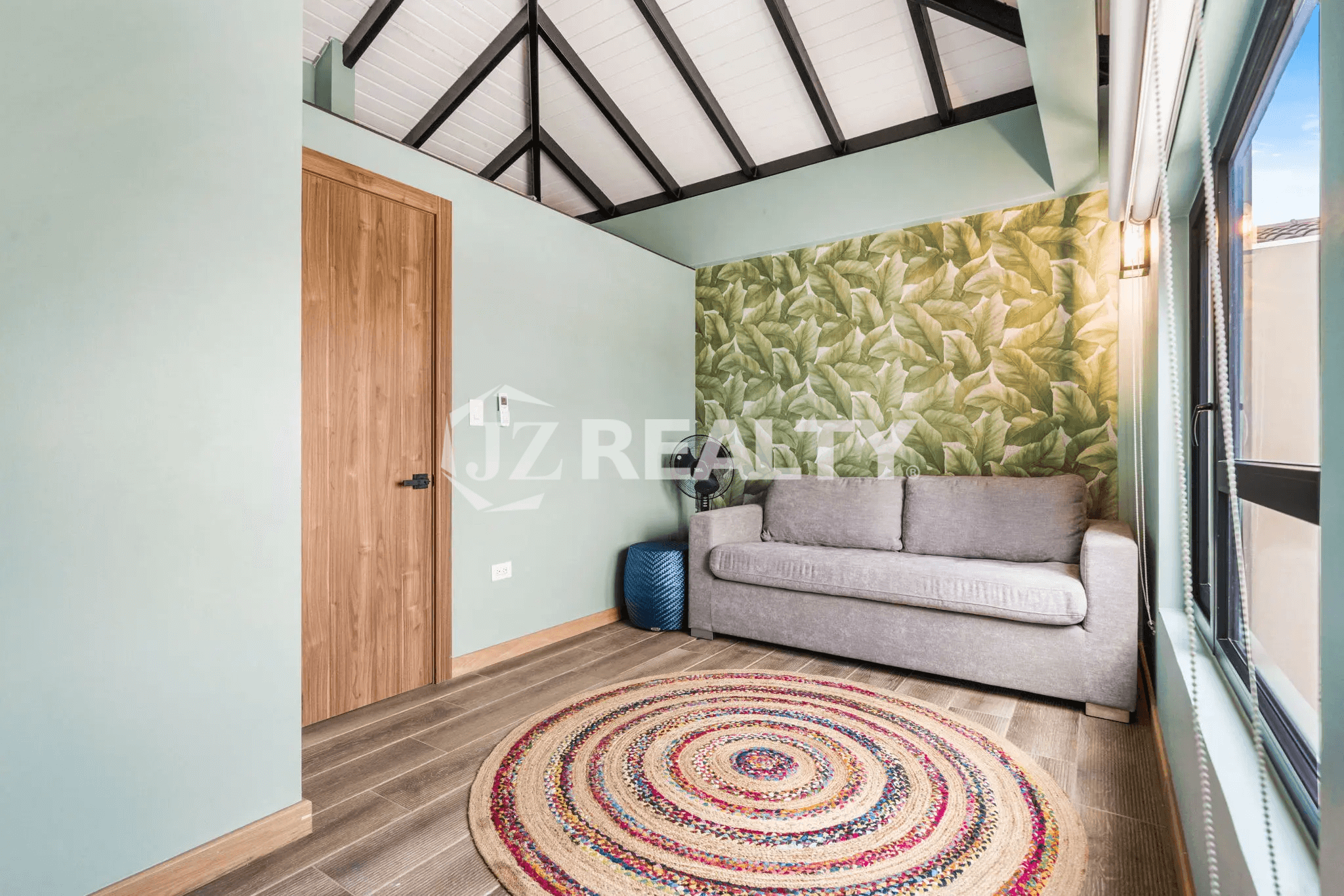 Cozy third-floor sitting room in Porta al Sole Unit 18 with a pull-out sofa, tropical leaf-patterned accent wallpaper, vaulted ceiling, and colorful circular rug.