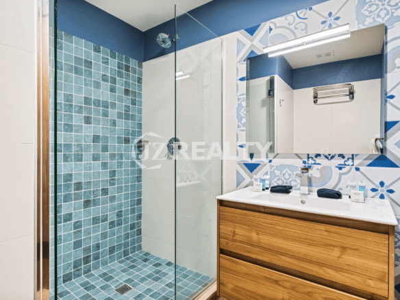 Modern bathroom in Porta al Sole Unit 8 with blue and white tile, a walk-in glass shower, and a wooden vanity with a single sink.