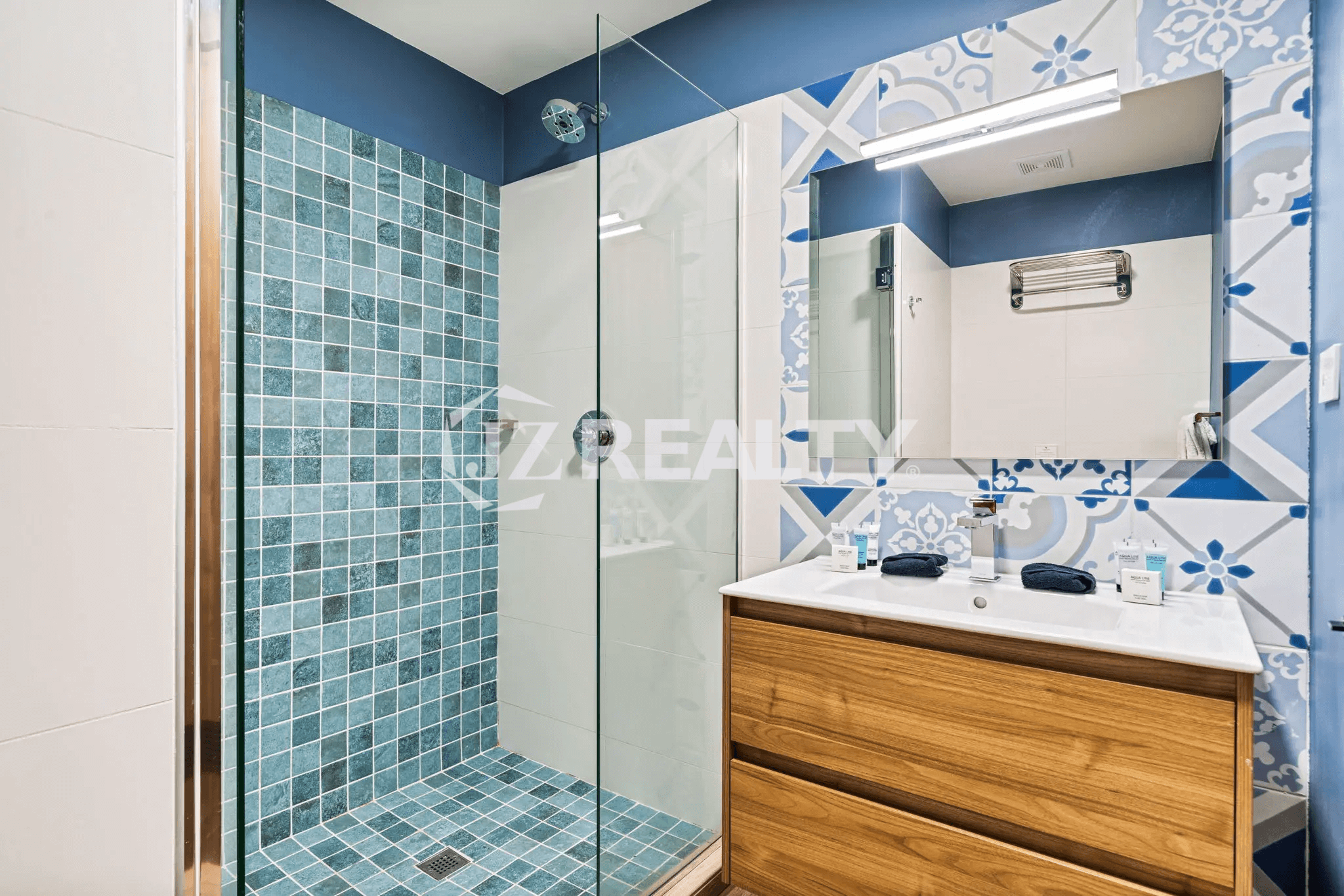 Modern bathroom in Porta al Sole Unit 8 with blue and white tile, a walk-in glass shower, and a wooden vanity with a single sink.