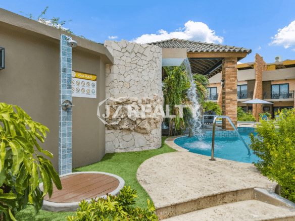 Outdoor shower area with stone accents and tropical landscaping near the entrance to the community pool at Porta al Sole.