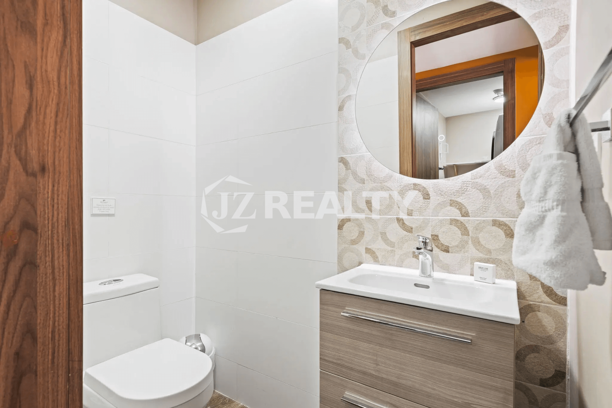 Powder room/half bath in Porta al Sole Unit 8 with a toilet, vanity, and a round mirrored wall design.