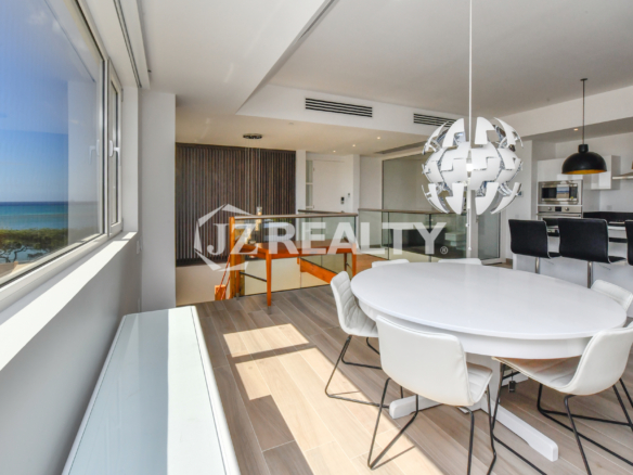 Bright and modern dining area at Coral Shell Condo 2E, featuring a sleek white round table, designer chandelier, and panoramic windows with ocean views.