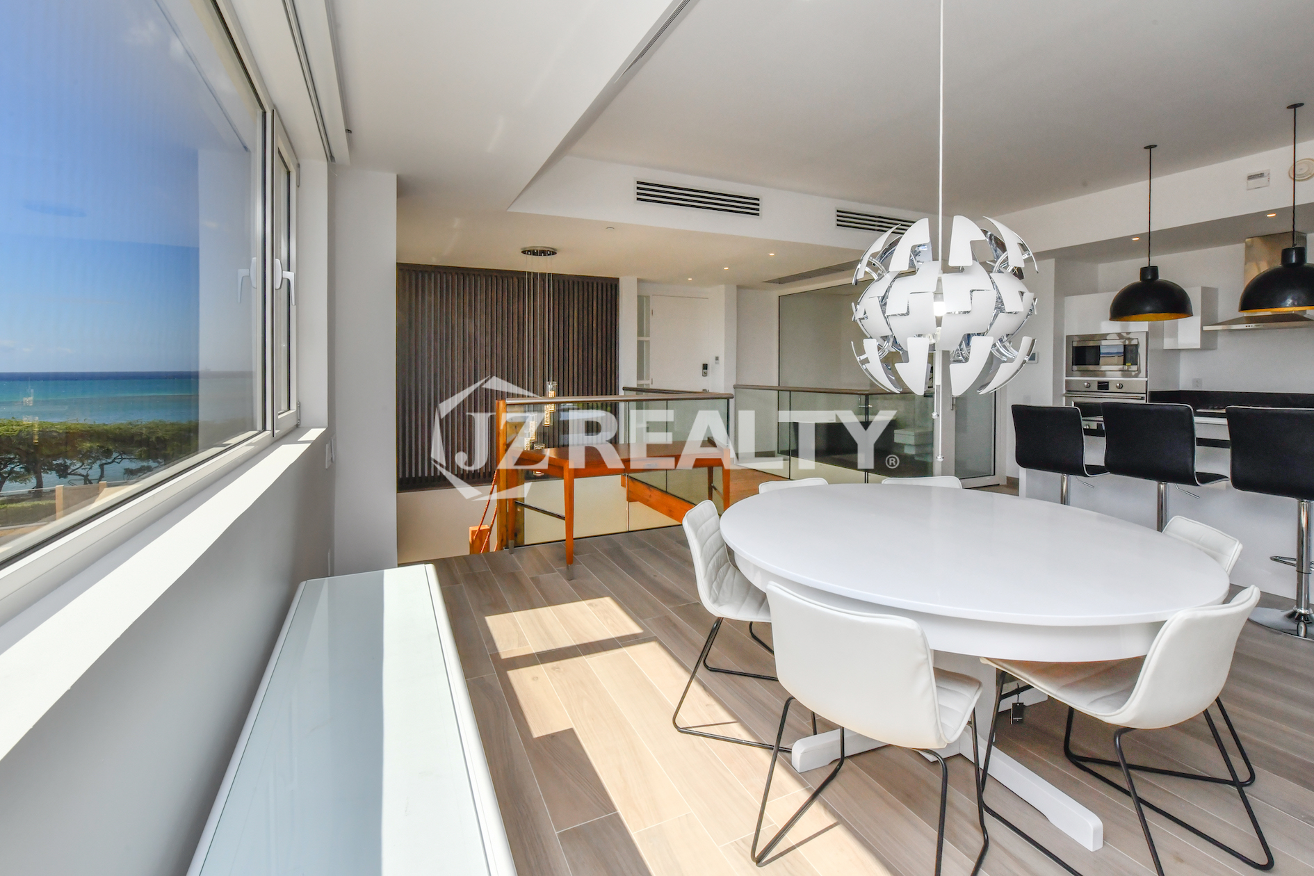 Bright and modern dining area at Coral Shell Condo 2E, featuring a sleek white round table, designer chandelier, and panoramic windows with ocean views.