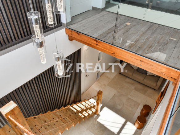 Modern loft-style staircase in Coral Shell Condo 1E, featuring wooden steps, glass railings, and high ceilings