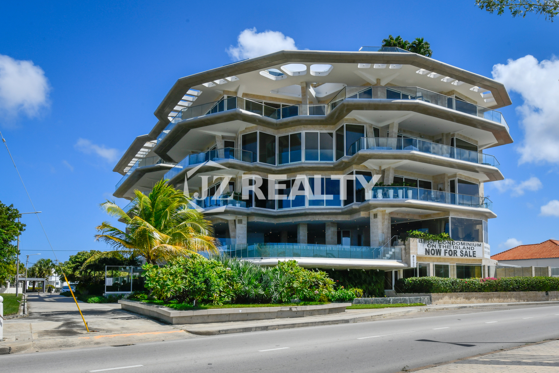 The modern and architecturally unique Coral Shell Condo in Aruba, captured from a street view, showcasing its luxurious beachfront design.