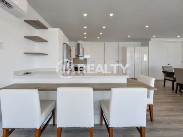 Modern living room with a flat-screen TV and open kitchen in Condo 1H, Coral Shell Condominium, Aruba.