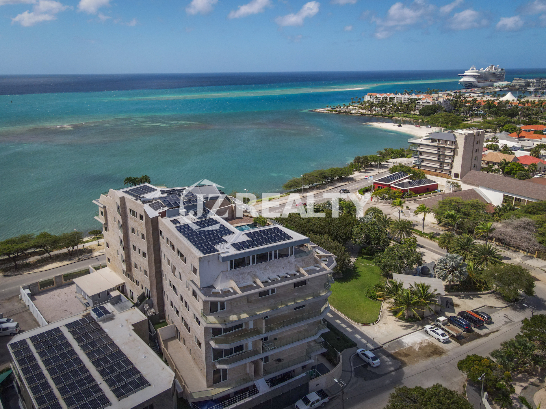 A stunning aerial view of Coral Shell Condo in Oranjestad, Aruba, with the Caribbean Sea and a cruise ship in the background.