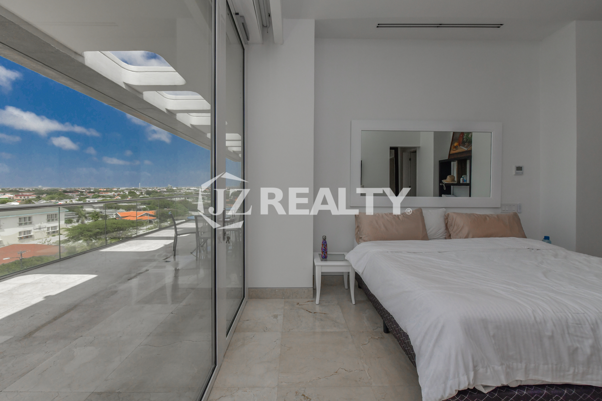 Luxury bedroom with floor-to-ceiling windows and island views at Coral Shell Penthouse B, Aruba.