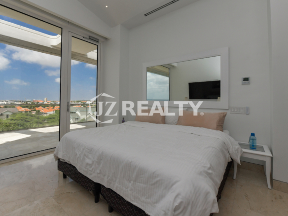 Luxurious bedroom with a spacious balcony and breathtaking ocean and city views at Coral Shell Penthouse B, Aruba.