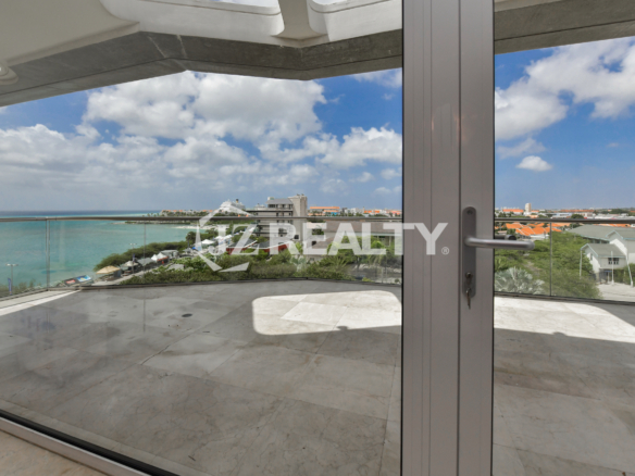 Luxurious balcony at Coral Shell Penthouse B in Aruba, featuring a glass railing, marble flooring, and breathtaking ocean and city views.