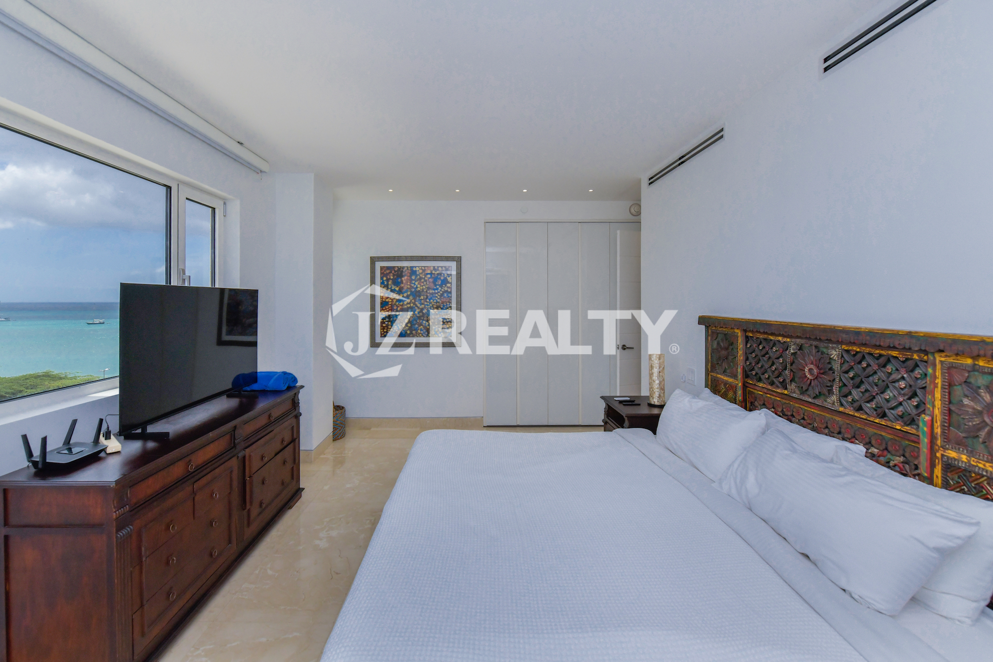 Stylish bedroom in Coral Shell Penthouse B featuring a custom-designed wooden headboard, crisp white linens, and an ocean-facing window.