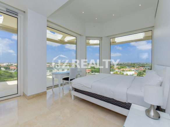 A bright and airy corner bedroom in Coral Shell Penthouse B with floor-to-ceiling windows offering panoramic city and ocean views.