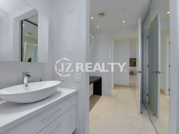 Modern vanity area leading to an ensuite bathroom in Coral Shell Penthouse B, featuring a sleek countertop, built-in shelves, and a large mirror.