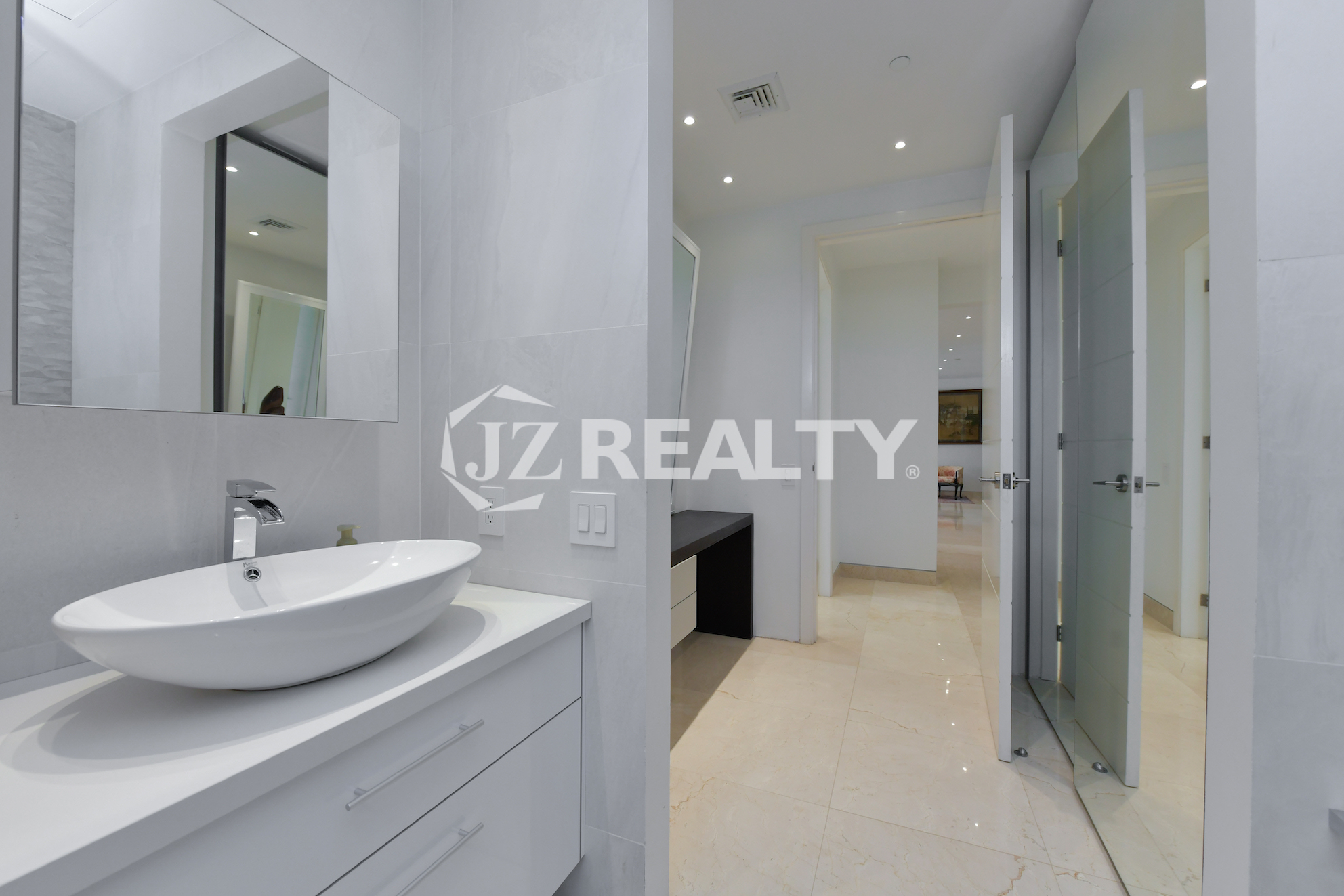 Modern vanity area leading to an ensuite bathroom in Coral Shell Penthouse B, featuring a sleek countertop, built-in shelves, and a large mirror.