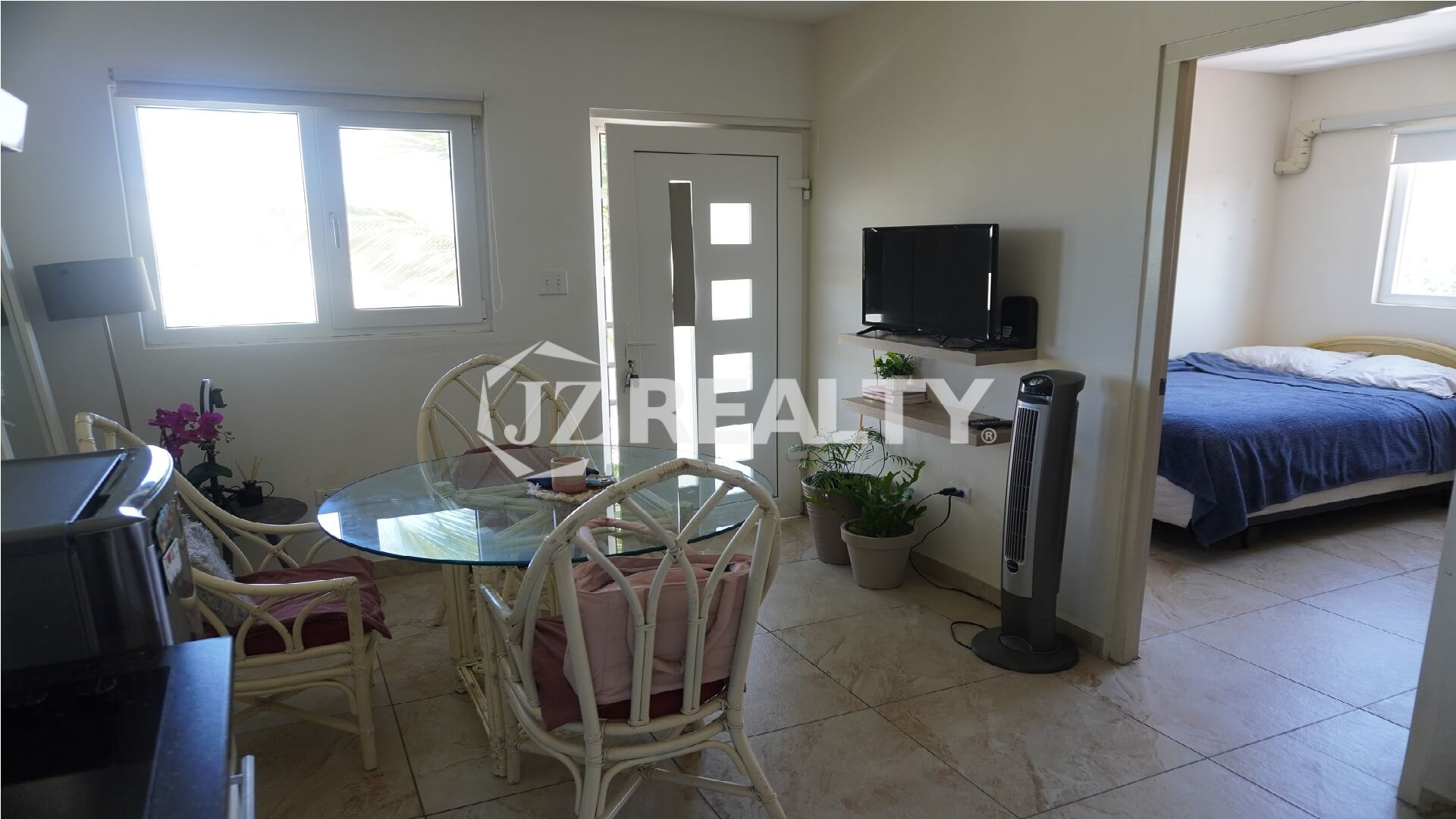 Open living and dining area with wall-mounted TV, plants and tiled floor.
