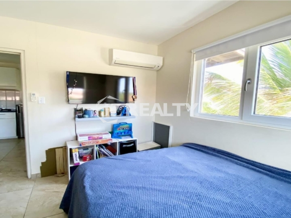 Bright bedroom with blue bedspread, window and wall-mounted air conditioner.