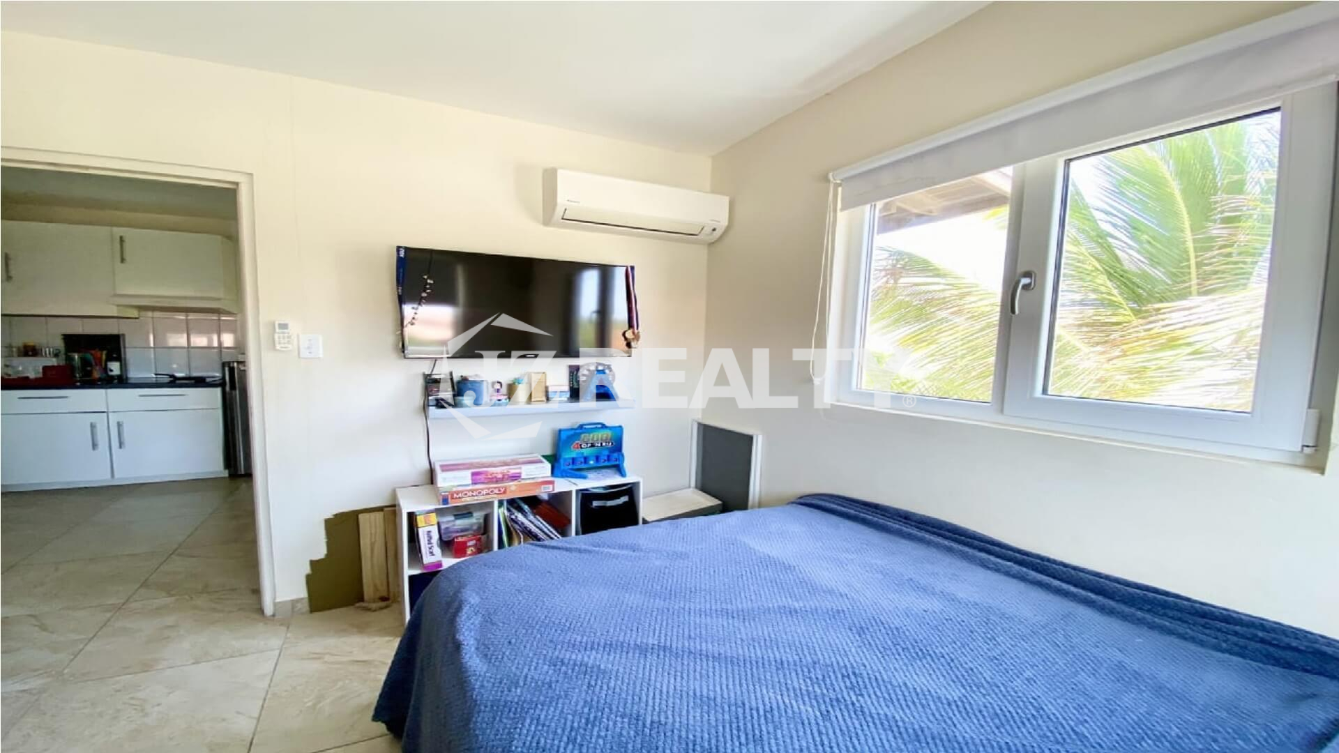 Bright bedroom with blue bedspread, window and wall-mounted air conditioner.