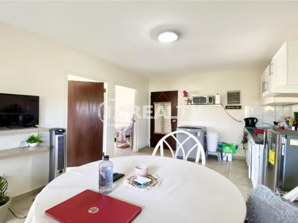 Compact kitchen and dining area with round table, refrigerator and white cabinets.