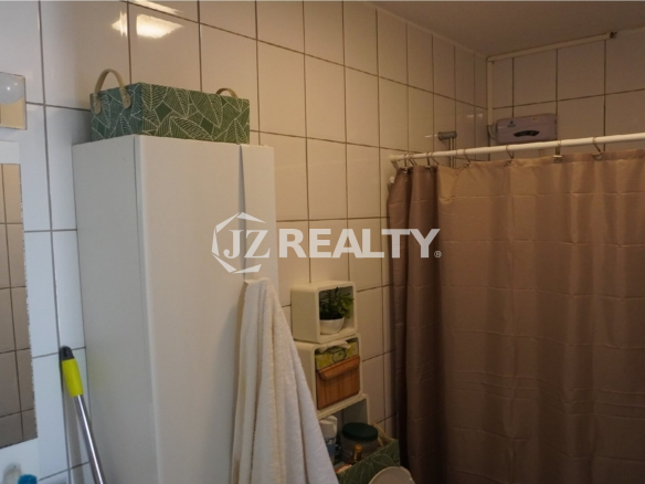 Compact bathroom with tiled walls, shower curtain and storage cabinet.