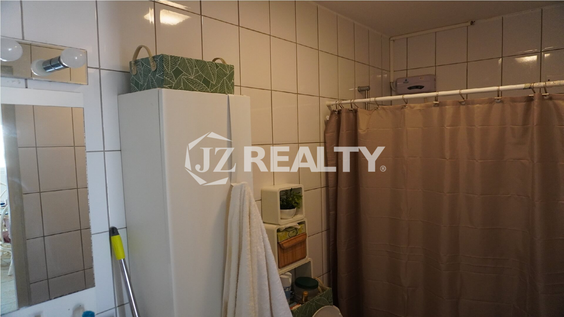 Compact bathroom with tiled walls, shower curtain and storage cabinet.