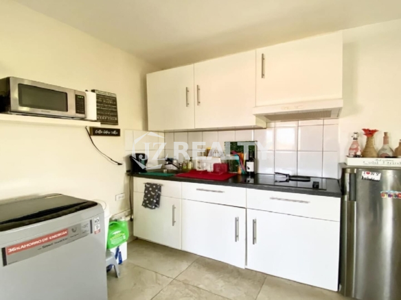 Modern kitchenette with white upper cabinets, black countertop and stainless fridge.