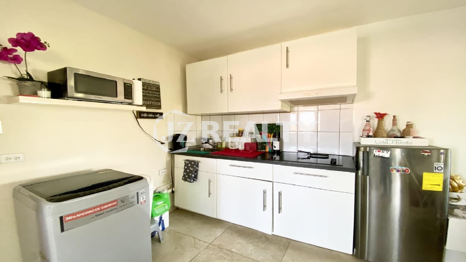 Modern kitchenette with white upper cabinets, black countertop and stainless fridge.