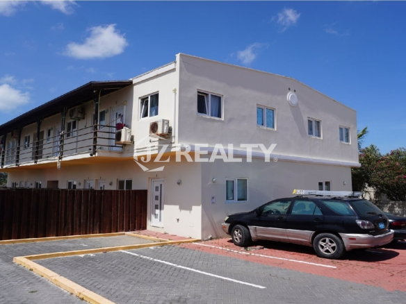 Two-story apartment building with parking bays and upper balconies under blue sky.