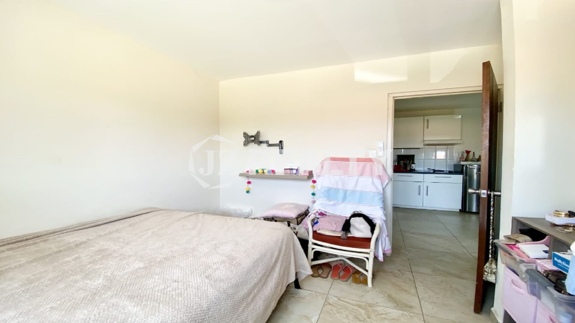 Small neutral bedroom showing doorway into kitchen and living area.