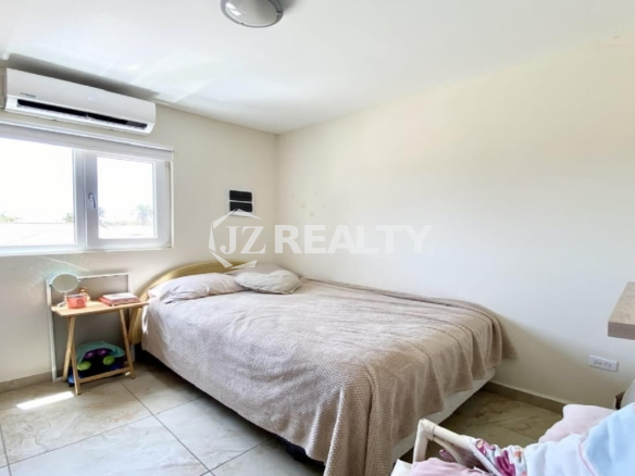 Cozy bedroom with beige bedspread, window and wall-mounted AC unit.