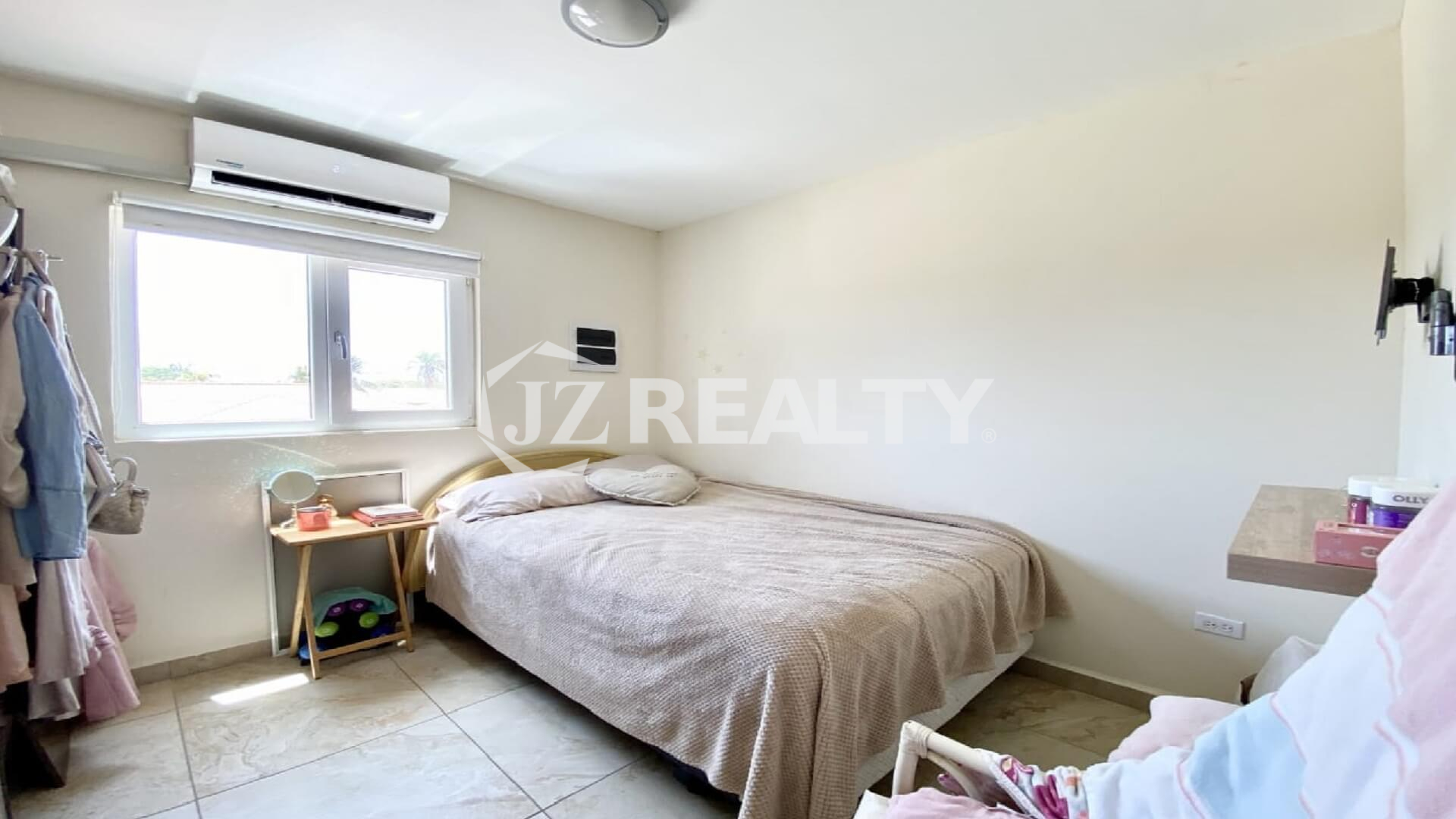 Cozy bedroom with beige bedspread, window and wall-mounted AC unit.