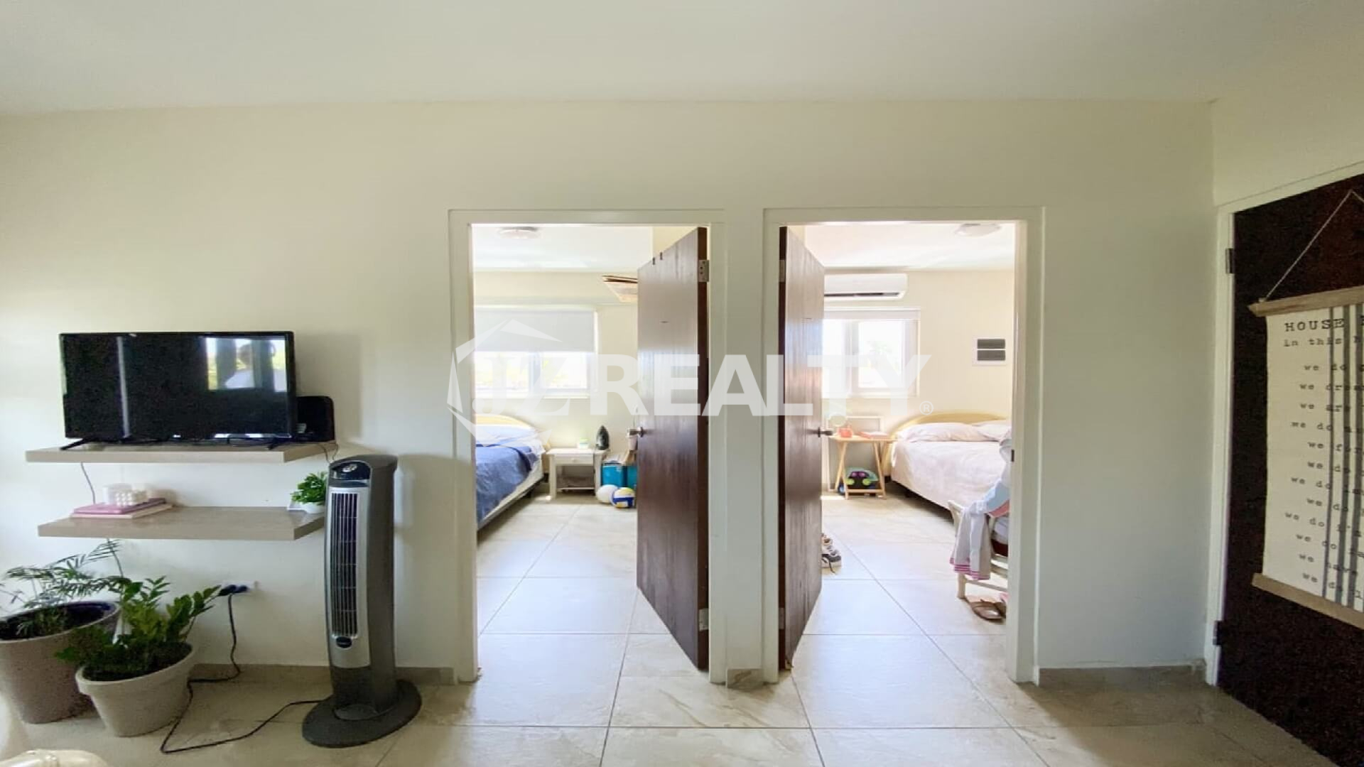 Shared hallway showing two open bedroom doors and wall-mounted TV in living area.