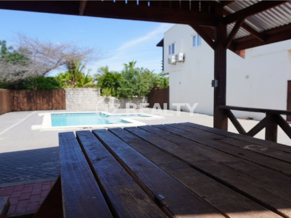 View of the pool from under a covered wooden gazebo with picnic table.