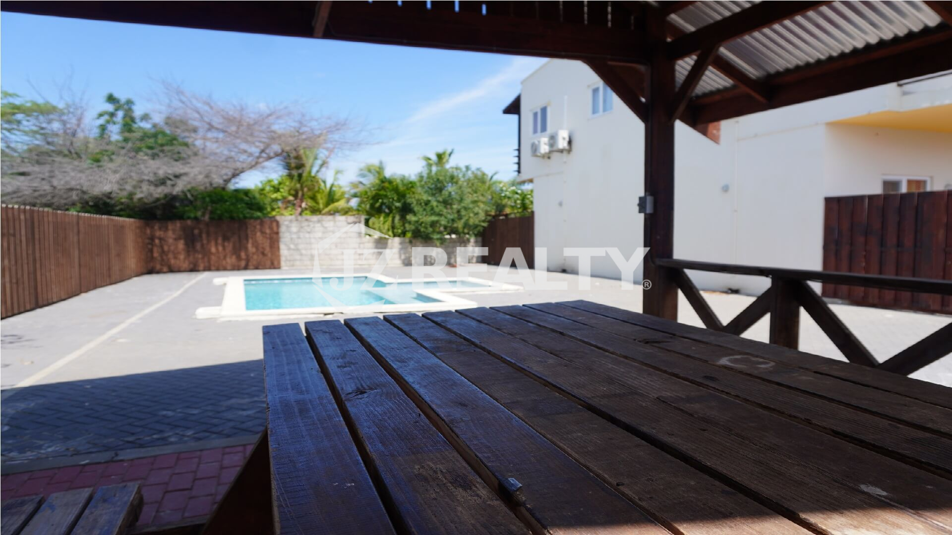 View of the pool from under a covered wooden gazebo with picnic table.