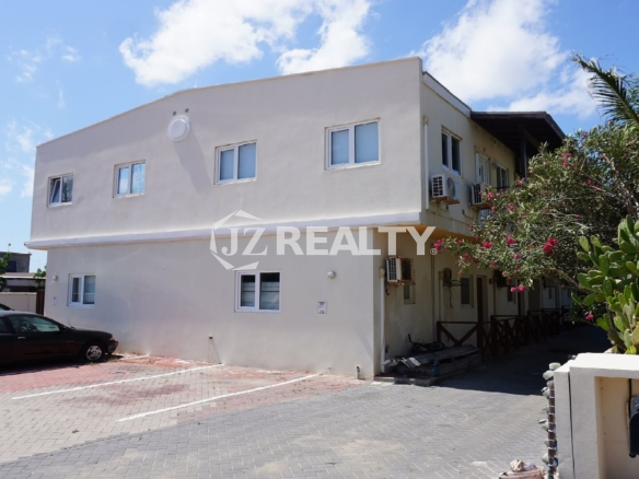 Exterior of two-story beige apartment building with private parking and garden plants.