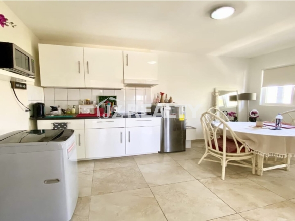 Bright kitchen with white cabinets, washing machine, and a small dining table beside a window.
