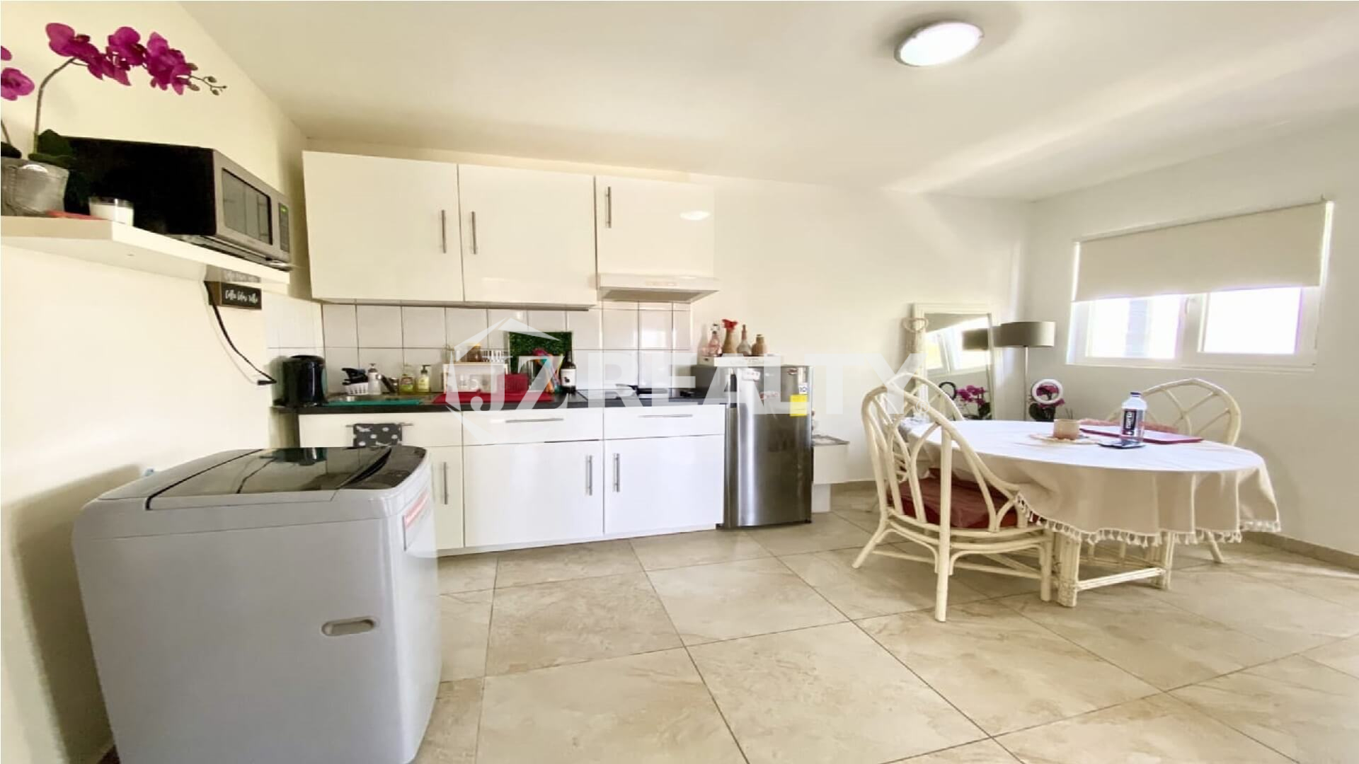 Bright kitchen with white cabinets, washing machine, and a small dining table beside a window.