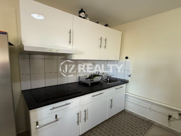 Close-up of the kitchen cabinetry, countertop, stovetop, and tiled backsplash.