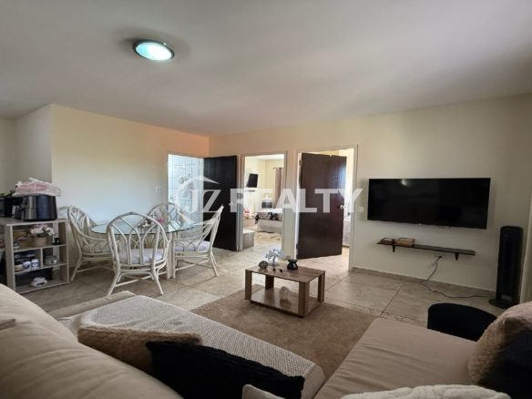 Wide-angle view of a furnished living room connected to a dining area with glass table and wicker chairs.