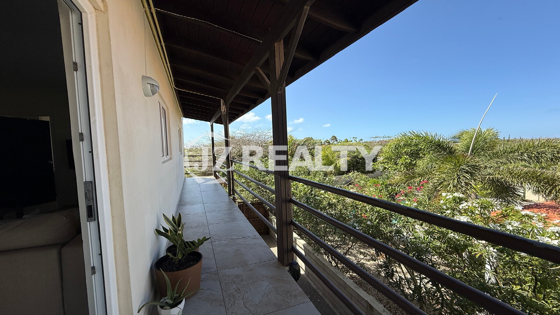 Outdoor walkway with potted plants and railing overlooking lush tropical greenery.